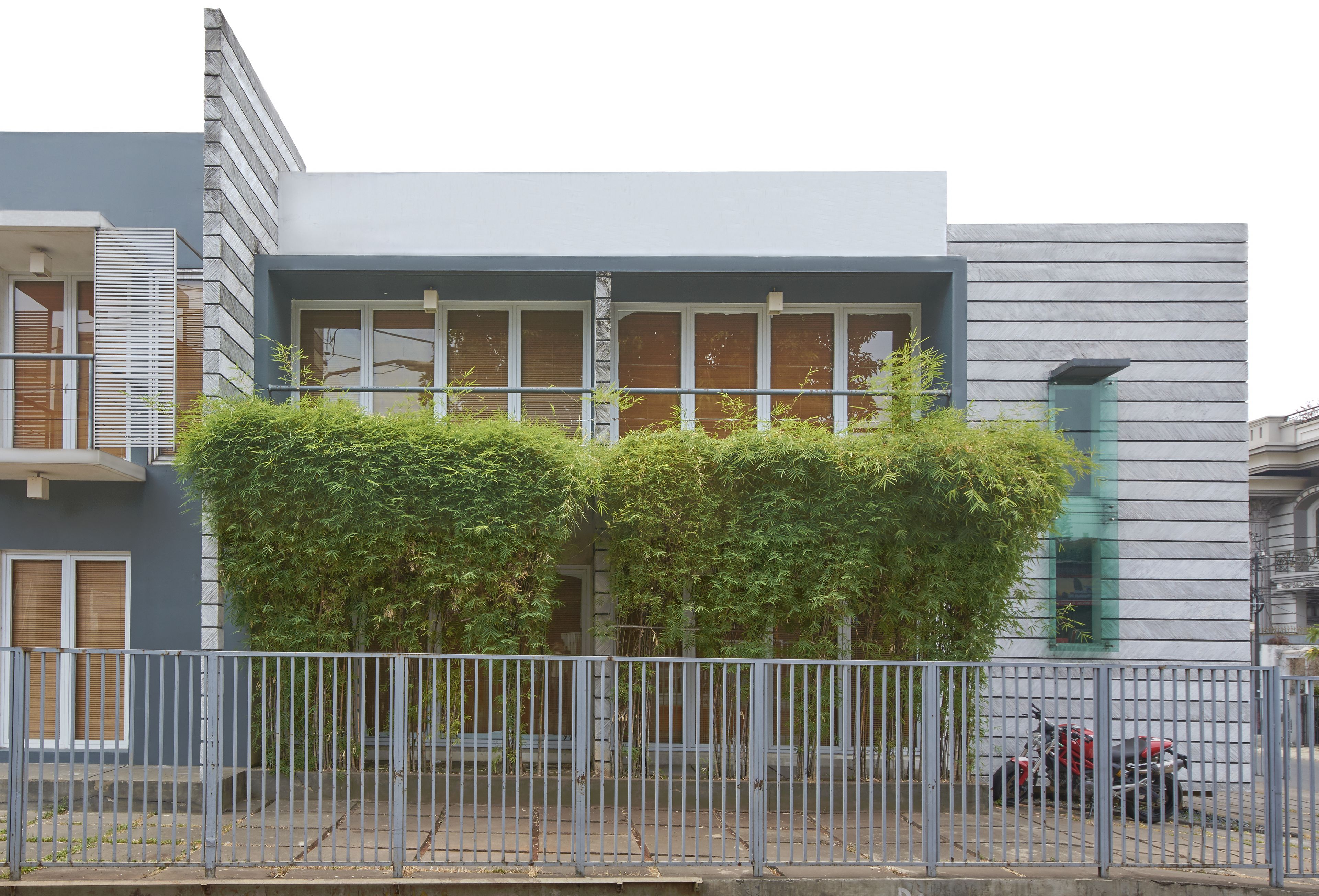 Un edificio moderno con tetto piatto, ampie finestre e una recinzione metallica di fronte.