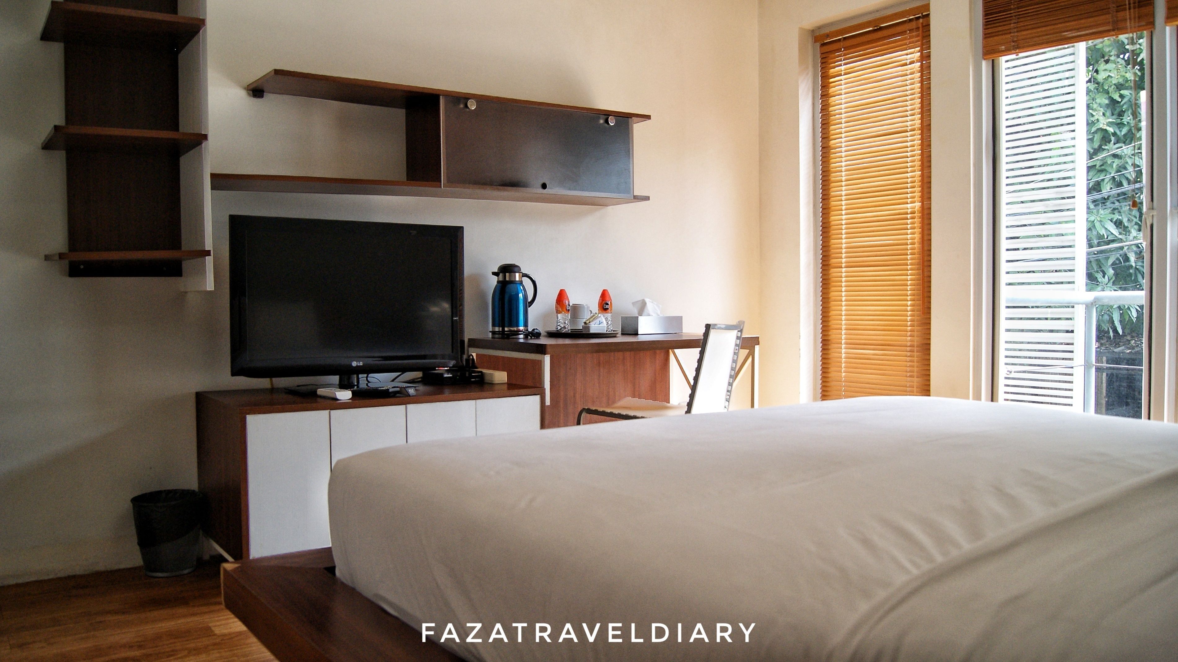 Un dormitorio con cama, televisión, cafetera y ventana con persianas.