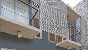 Un edificio moderno de dos pisos con balcón, ventanas grandes y fachada gris.