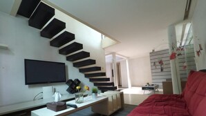 Una sala de estar moderna con un sofá rojo, un televisor de pantalla plana y una escalera con escalones negros.
