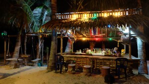 Un bar junto a la playa con techo de paja, asientos de madera y barra.