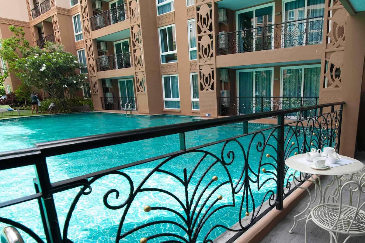 A balcony with a pool, white metal chairs, and a table with cups and saucers.