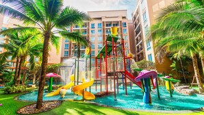 A water park with slides and a climbing structure, surrounded by palm trees and a building in the background. - Atlantis Residence - Huge Saltwater Waterpark, Gym & Kids Playground - Free Parking (Pattaya)