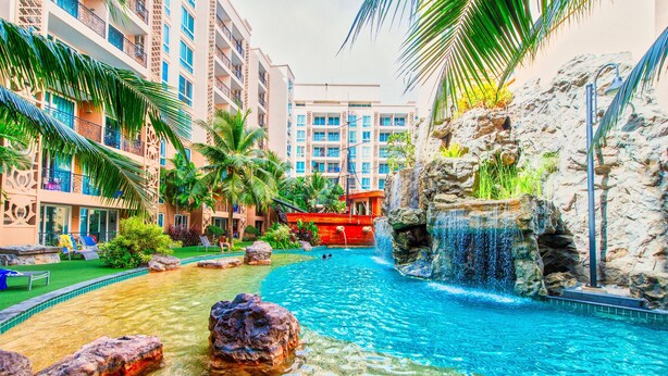 A hotel pool area with clear water, rocks, palm trees, and a waterfall. - Atlantis Residence - Huge Saltwater Waterpark, Gym & Kids Playground - Free Parking (Pattaya)