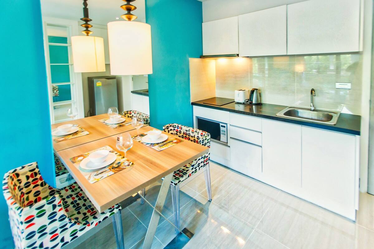 A modern kitchen with white cabinets, a stainless steel sink, and a wooden dining table set for four.