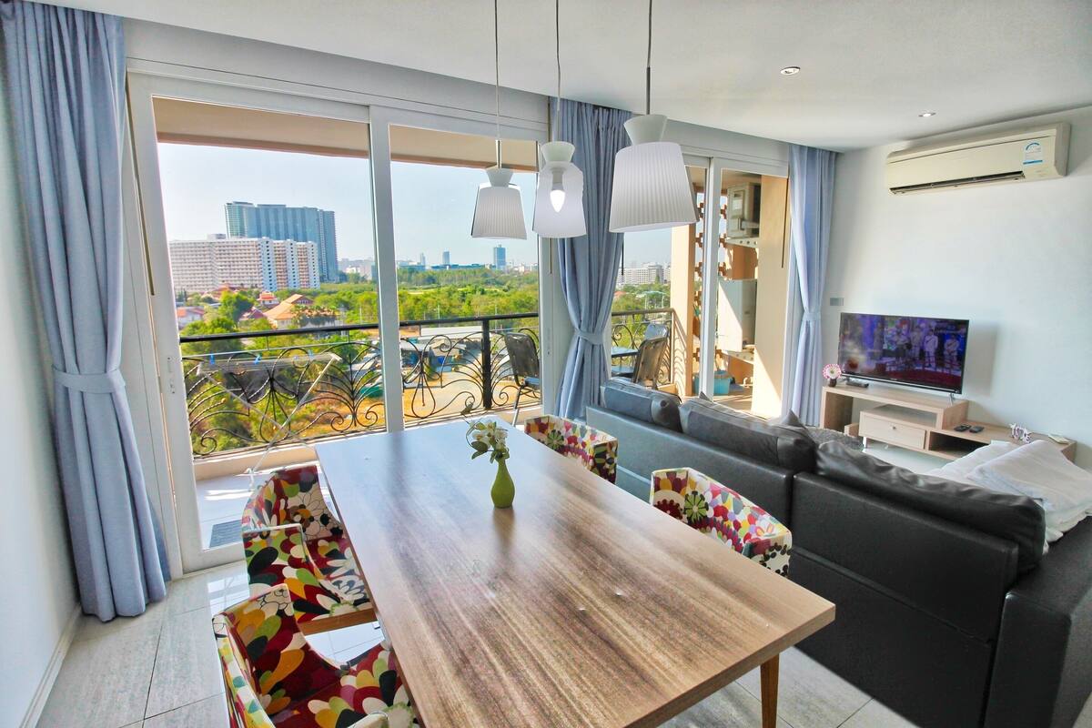 A modern living room with a wooden dining table, colorful chairs, a black sofa, and a TV.
