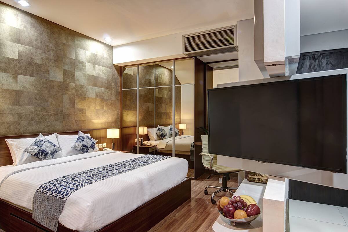 Ein Hotelzimmer mit einem großen Bett, einem Flachbildfernseher, einem Nachttisch mit Obstschale und einer Spiegelwand.