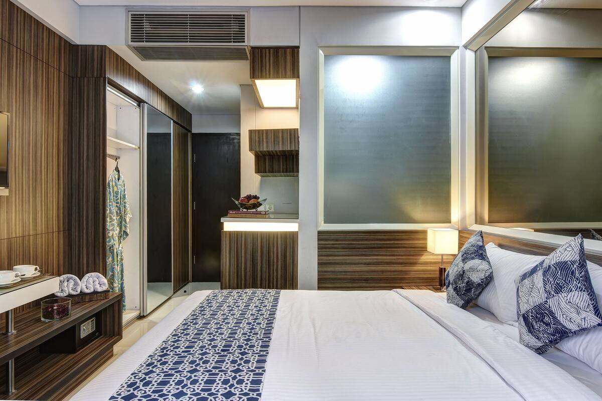 Ein modernes Hotelzimmer mit einem großen Bett, einem Schminktisch mit Spiegel, einem eingebauten Kleiderschrank und einer kleinen Küchenzeile.