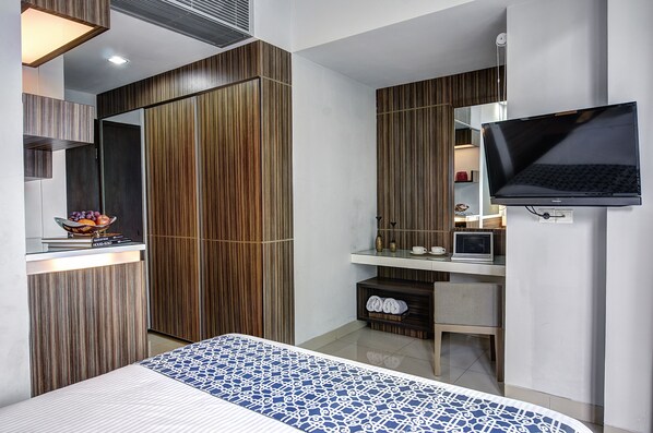 A modern bedroom with a bed, a TV, a desk with a laptop, and a wardrobe.
