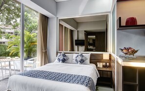 A hotel room with a large bed, a bedside table with a lamp, a TV mounted on the wall, and a view of greenery outside.