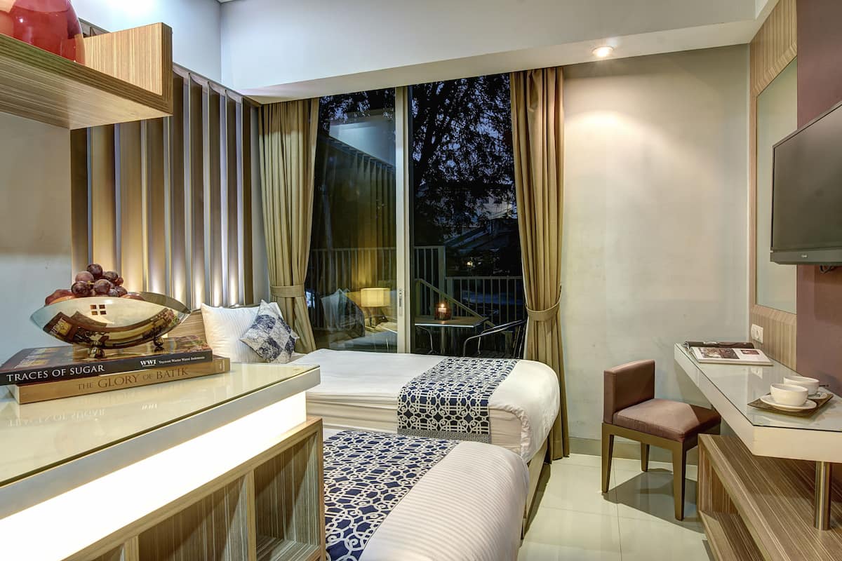 Ein Hotelzimmer mit zwei Betten, einem Schreibtisch mit Stuhl, einem Fernseher und einem Balkon mit Tisch und Stühlen.
