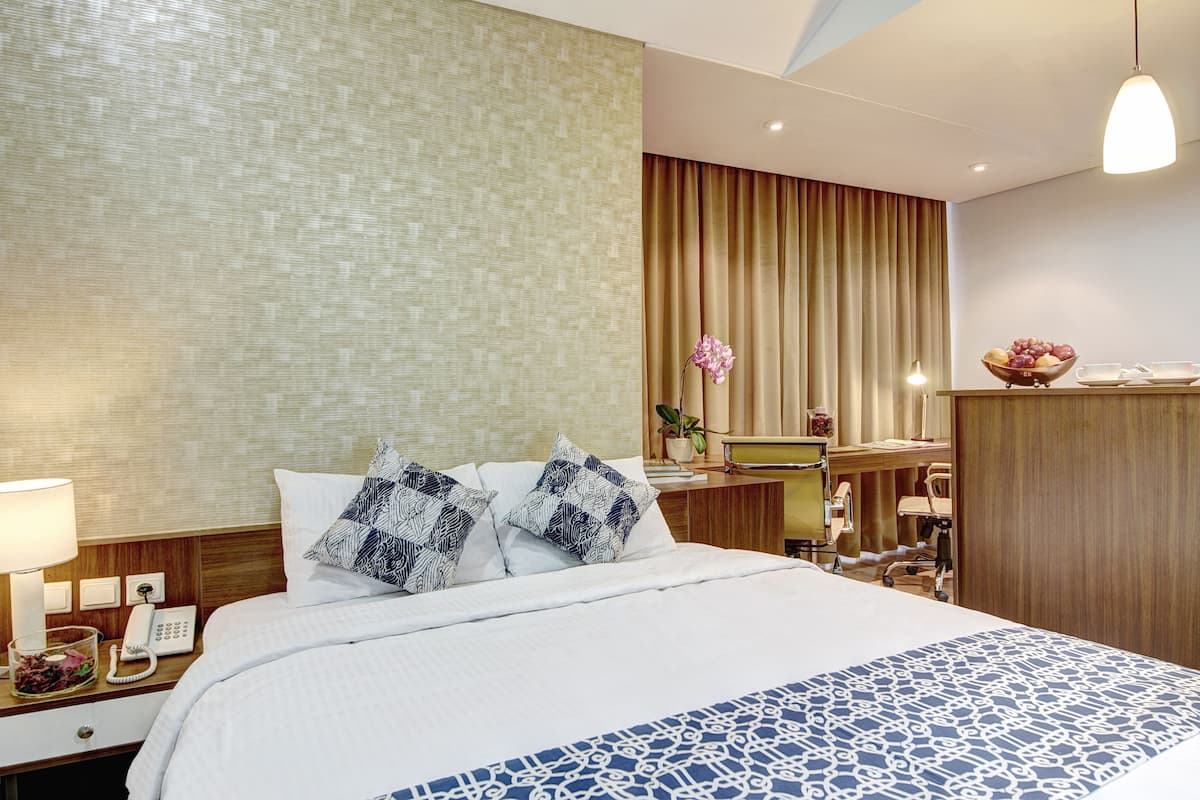 Ein Hotelzimmer mit einem großen Bett, einem Schreibtisch mit Computer, einem Telefon und einem kleinen Tisch mit einer Obstschale.