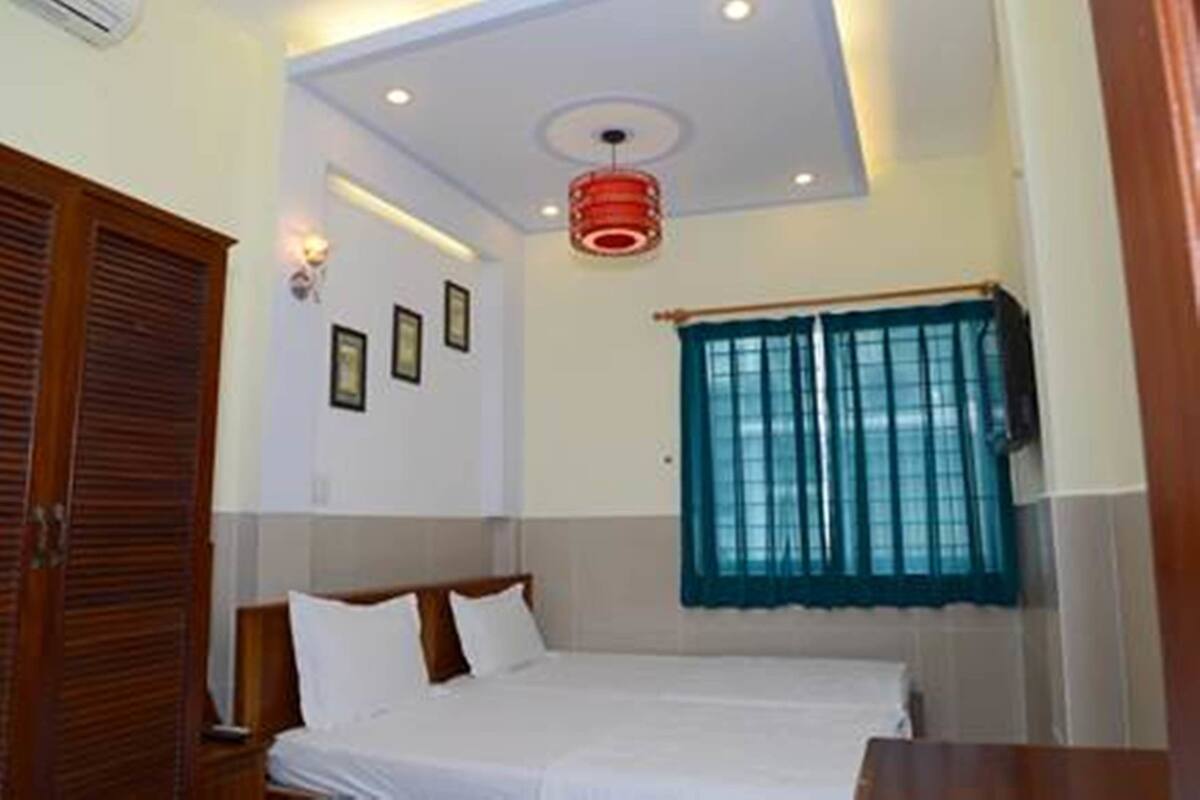A hotel room with a bed, a wardrobe, a window with curtains, and a ceiling light fixture.