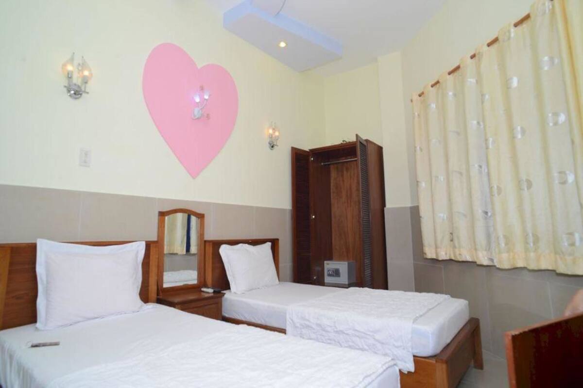 A hotel room with two beds, a wooden wardrobe, a large mirror, and a decorative heart on the wall.