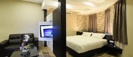 A modern hotel room with a bed, a TV, a desk, and a stone wall.