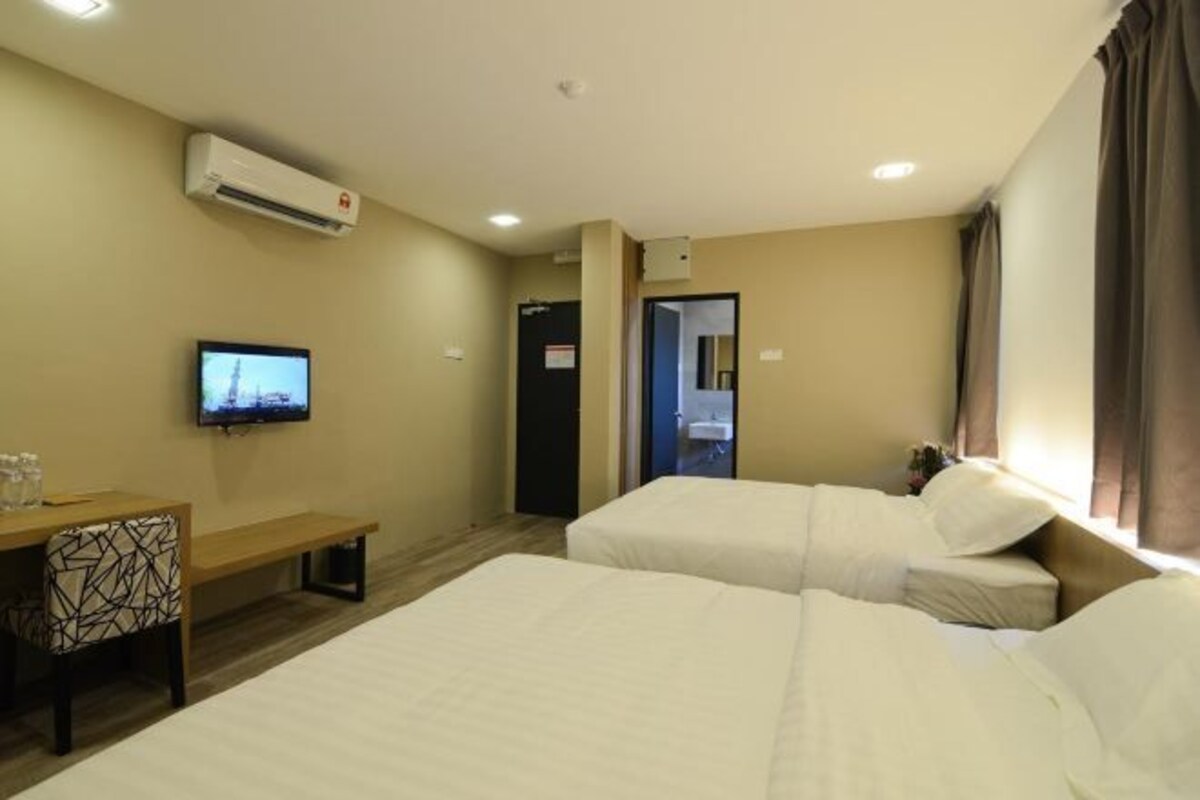 A hotel room with two beds, a desk with a chair, a television, and an air conditioning unit.