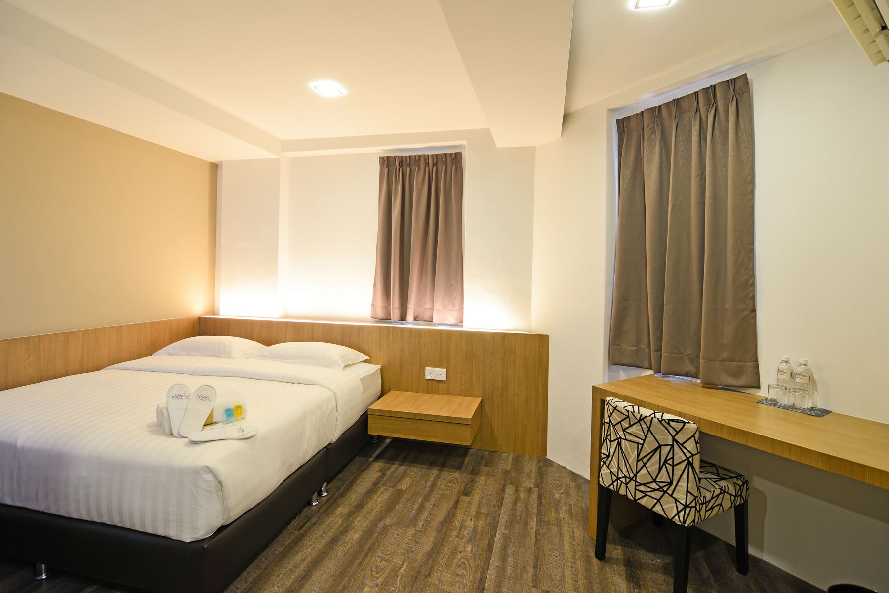 A hotel room with a bed, bedside table, chair, and a desk with a mirror.