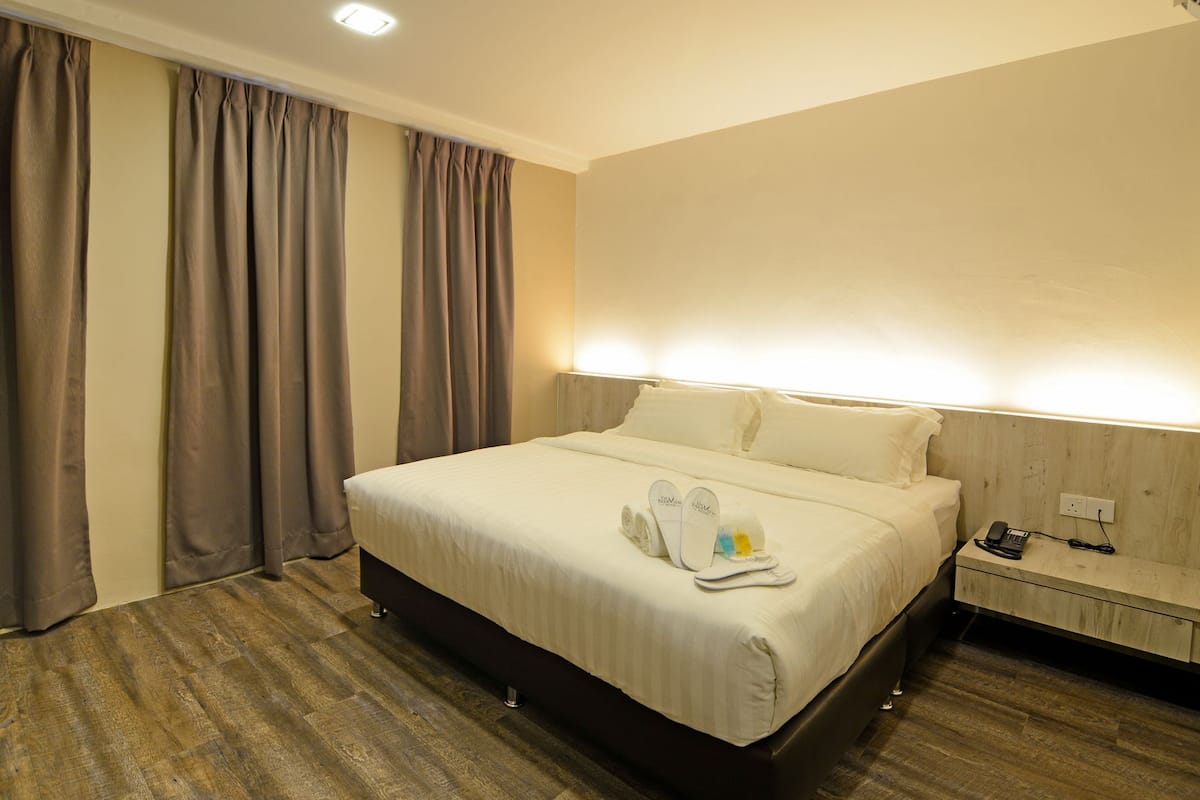 A hotel room with a large bed, a bedside table with a phone and charger, and a nightstand with a lamp.