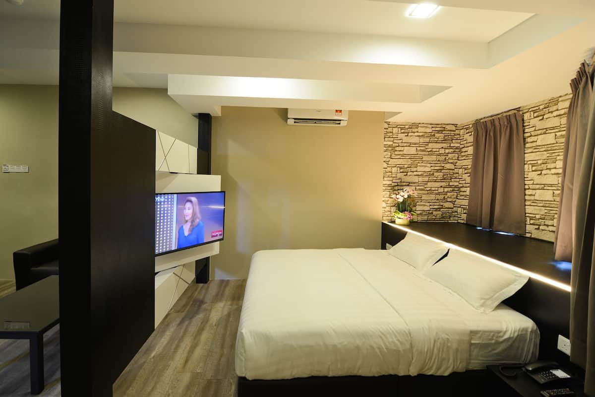 A modern hotel room with a large bed, a flat-screen TV mounted on the wall, a stone accent wall, and a small table with a vase of flowers.