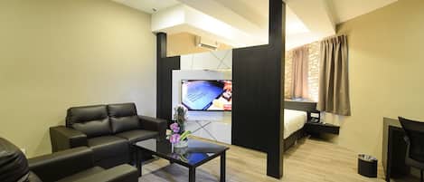 A modern hotel room with a sofa, a coffee table with flowers, a TV, a bed, and a desk.