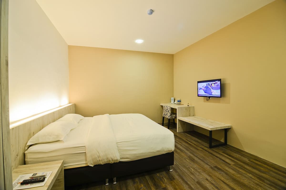 A hotel room with a bed, a desk, a chair, a TV, and a nightstand.