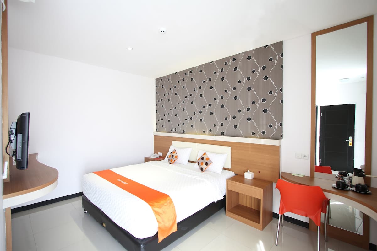 Una habitación de hotel moderna con una cama bien hecha, un escritorio con una silla, un espejo grande y un televisor sobre un mueble.