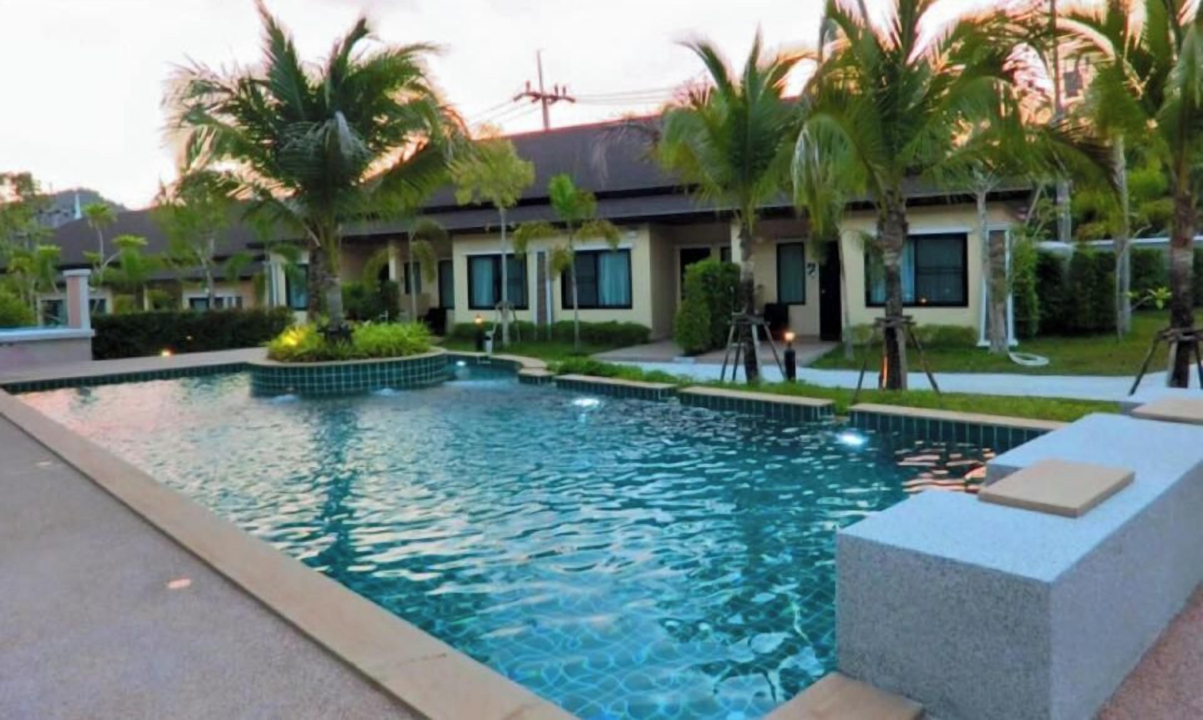 A swimming pool with a clear blue water surface, surrounded by palm trees and a building with multiple windows.