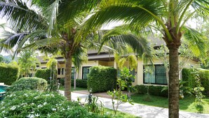 A hotel with a well-maintained garden, palm trees, and a pathway leading to the entrance.