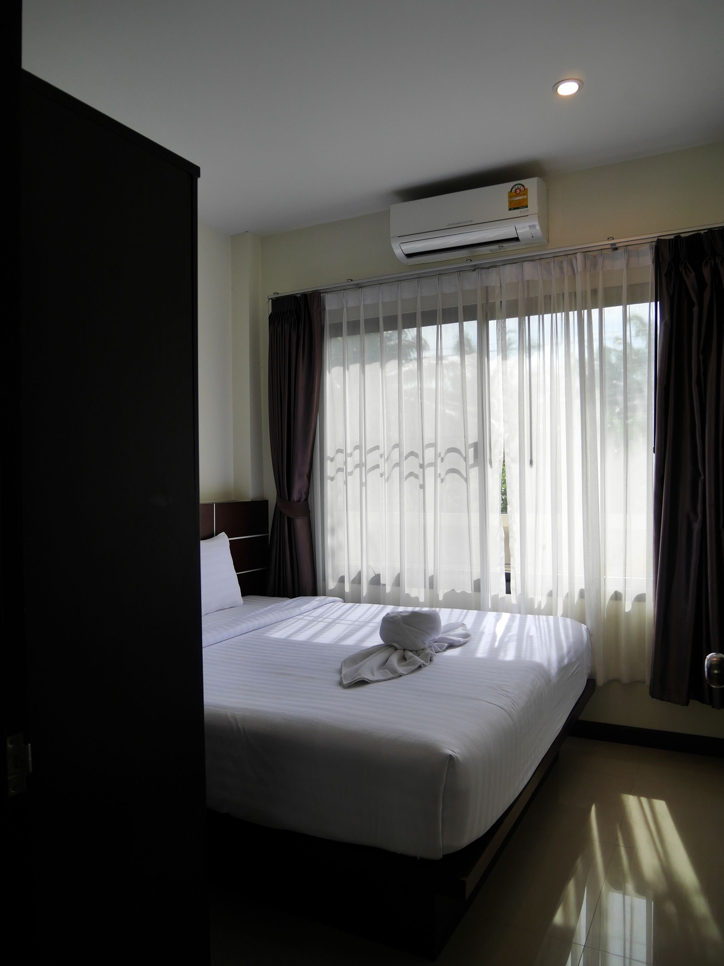 Ein Hotelzimmer mit einem großen Bett, einer Klimaanlage, durchsichtigen Vorhängen und Blick ins Freie.