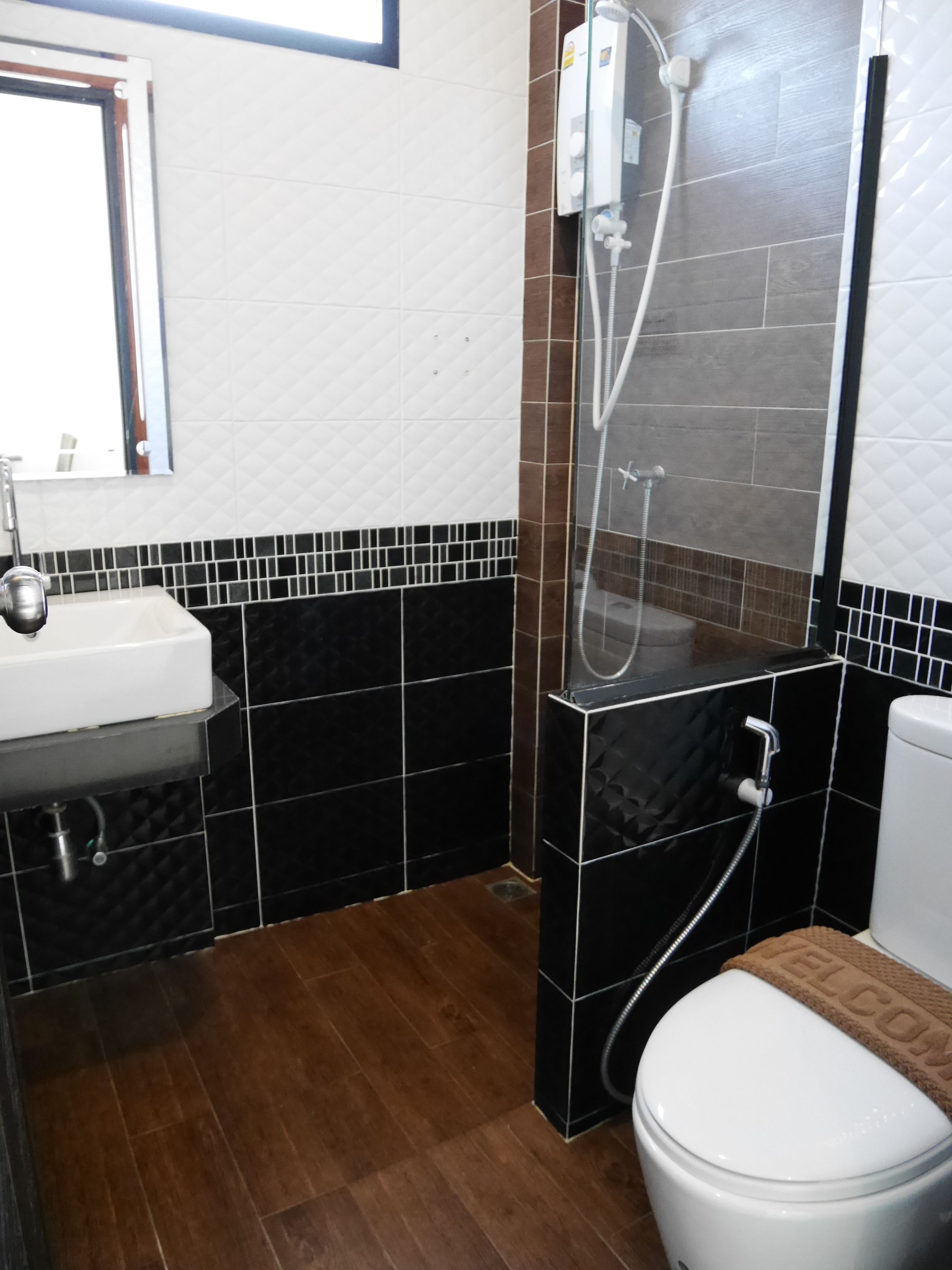 Un baño con un lavamanos blanco, paredes con azulejos blanco y negro, una cabina de ducha y un inodoro con una alfombra marrón.