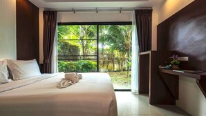 A modern hotel room with a large bed, a view of greenery through the glass door, and a small desk with a plant.