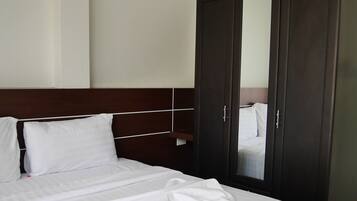 A neatly made bed with white linens and a folded towel, a dark wooden wardrobe, and a wall-mounted air conditioning unit.