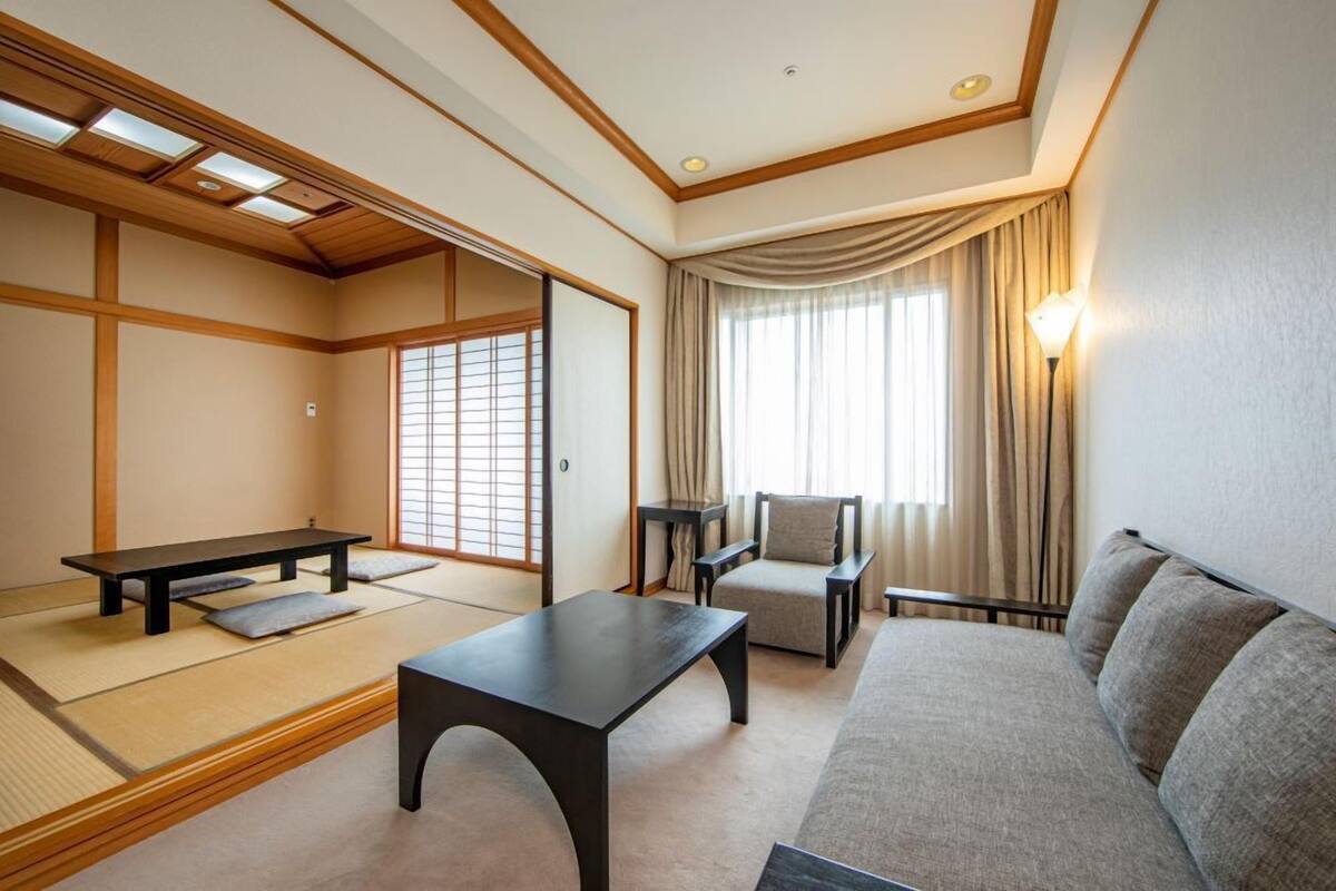 A traditional Japanese room with tatami flooring, a low table, a sofa, a chair, and a sliding door.