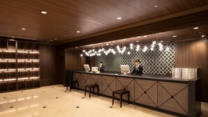 Uma área de recepção com um balcão de madeira, dois monitores de computador e um painel de parede estampado.