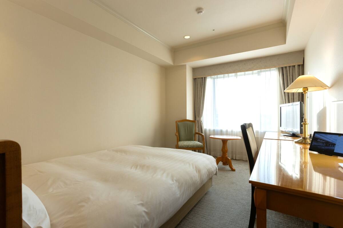 A hotel room with a single bed, a desk with a laptop, a chair, and a small table.