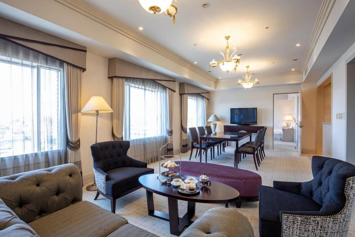 A hotel room with a seating area, a dining table, and a television.