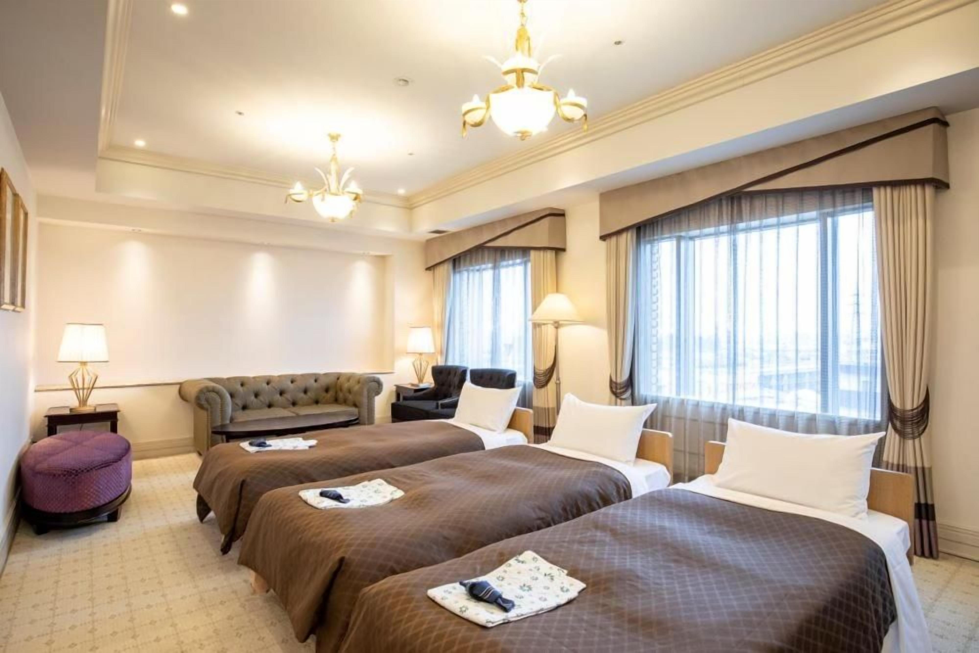 A hotel room with two beds, a sofa, a small table, and a lamp.
