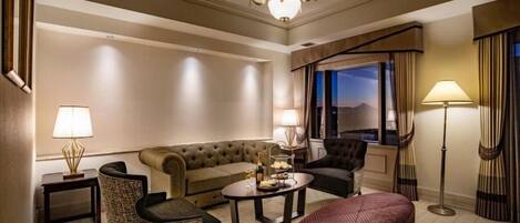 A hotel room with a sofa, armchairs, a coffee table, a floor lamp, and a view of the outdoors.