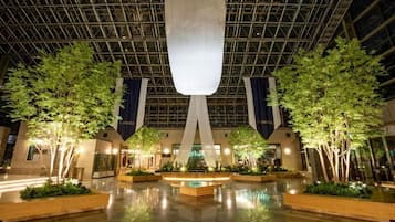 A spacious indoor atrium with a high ceiling, large windows, and a central water feature.