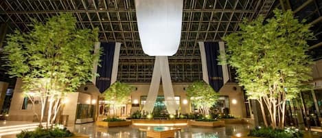 A spacious indoor atrium with a high ceiling, large windows, and a central water feature.