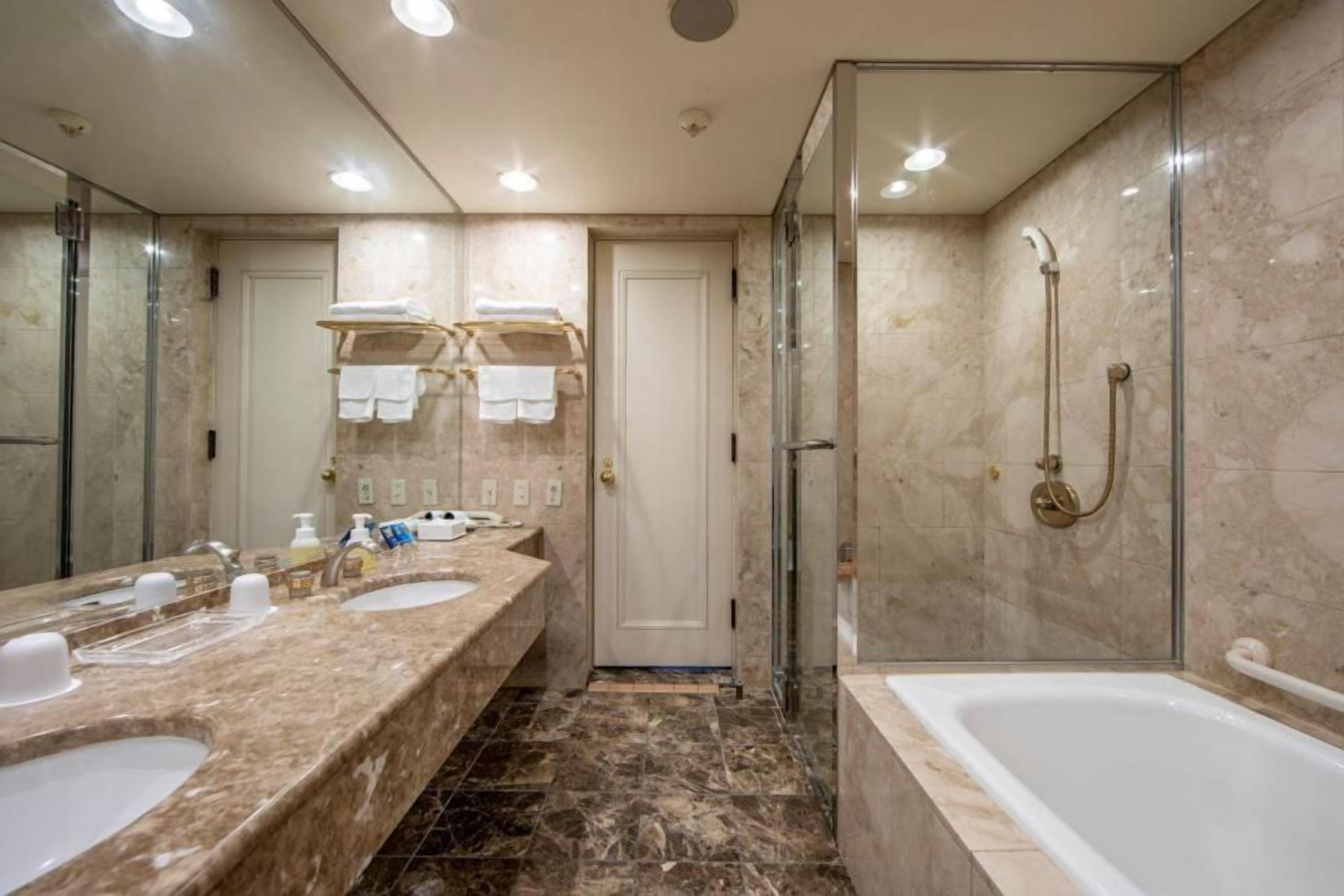 A modern bathroom with two sinks, a glass-enclosed shower, and a bathtub.
