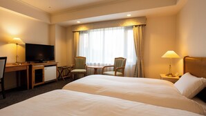 Quarto de hotel com uma cama grande, uma mesa com televisão, duas cadeiras, uma mesinha e uma mesa de cabeceira com abajur.