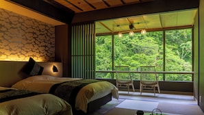 Une chambre avec deux lits, une vue sur une forêt grâce à de grandes fenêtres, un balcon avec une chaise et une petite table avec une théière et une tasse.