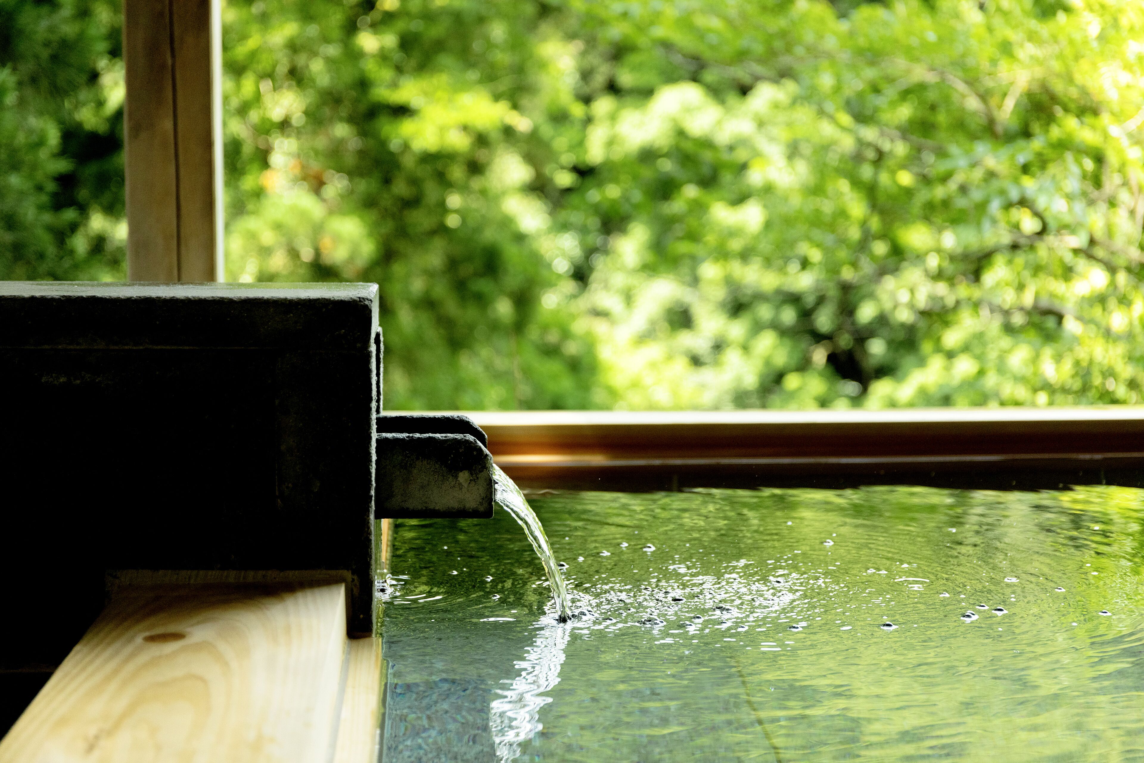 Eine Holzkonstruktion mit Wasserspiel, Fenster und Blick ins Grüne.