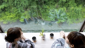 Deux personnes sont assises à une table, devant laquelle s’étend un paysage offrant une vue sur une rivière et une végétation luxuriante.