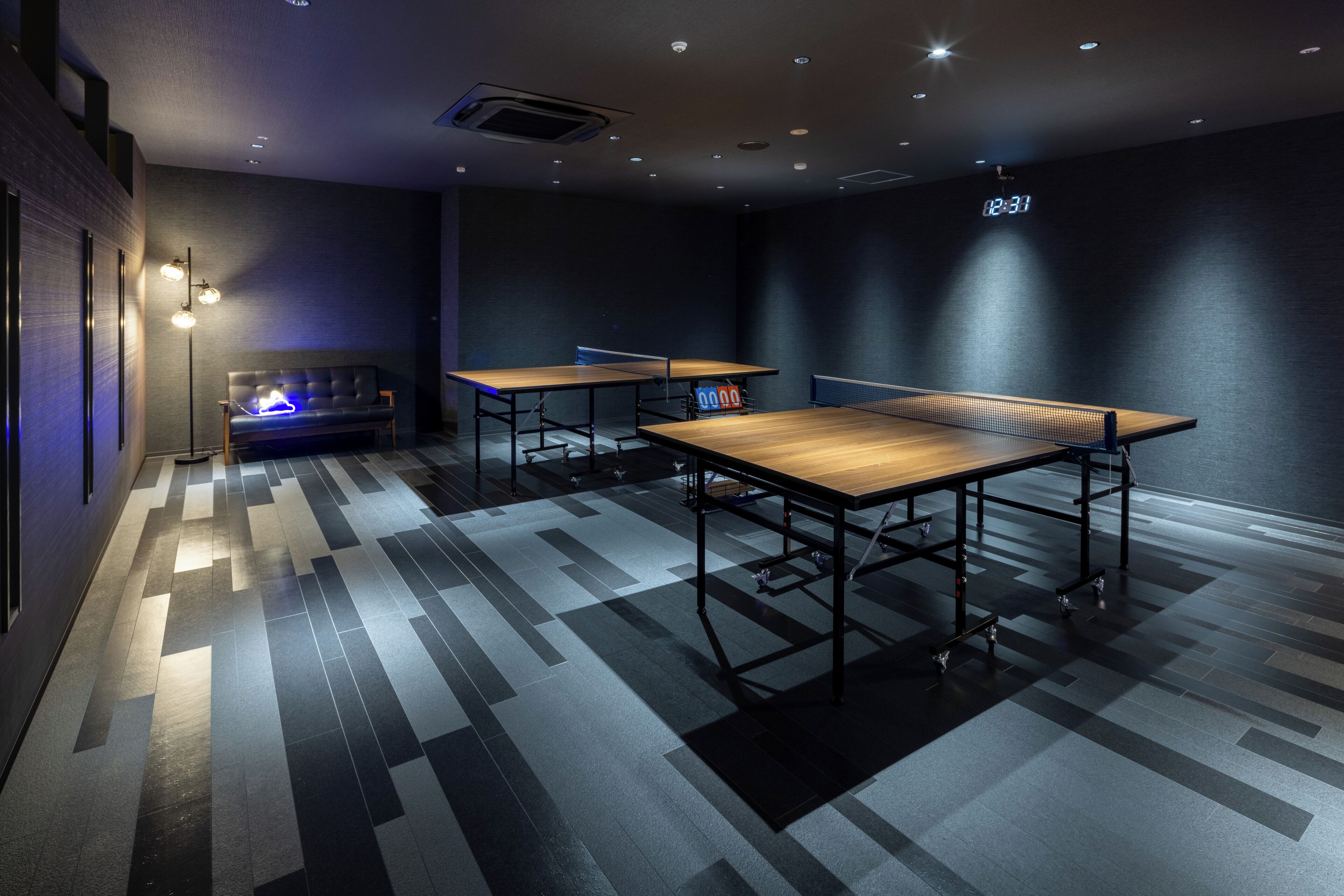 Een moderne kamer met twee tafeltennistafels, een bank en een digitale klok aan de muur.