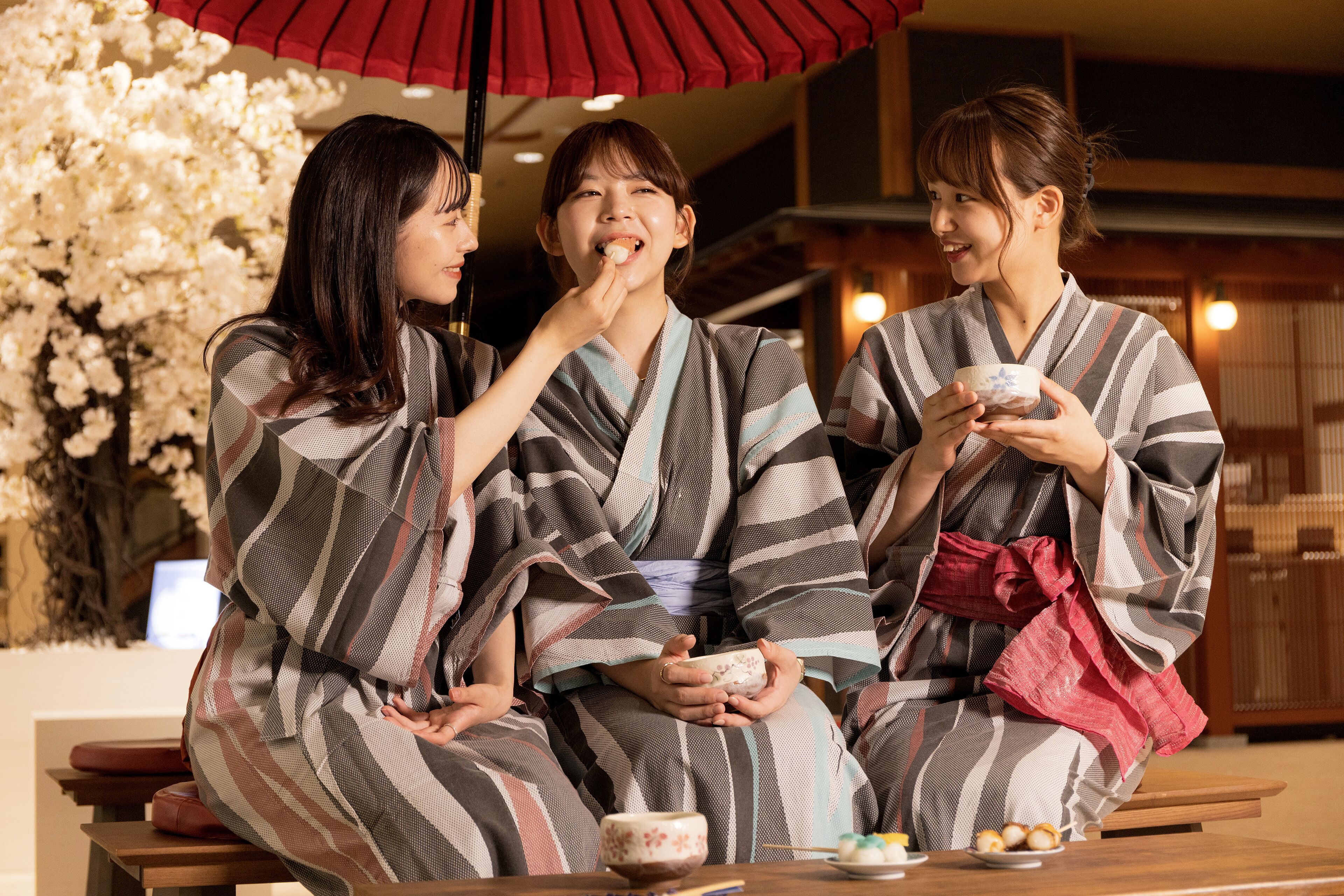Three people in traditional Japanese attire sitting at a table with a floral backdrop.