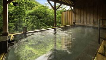 A hot spring bath with a wooden structure and a view of lush greenery.