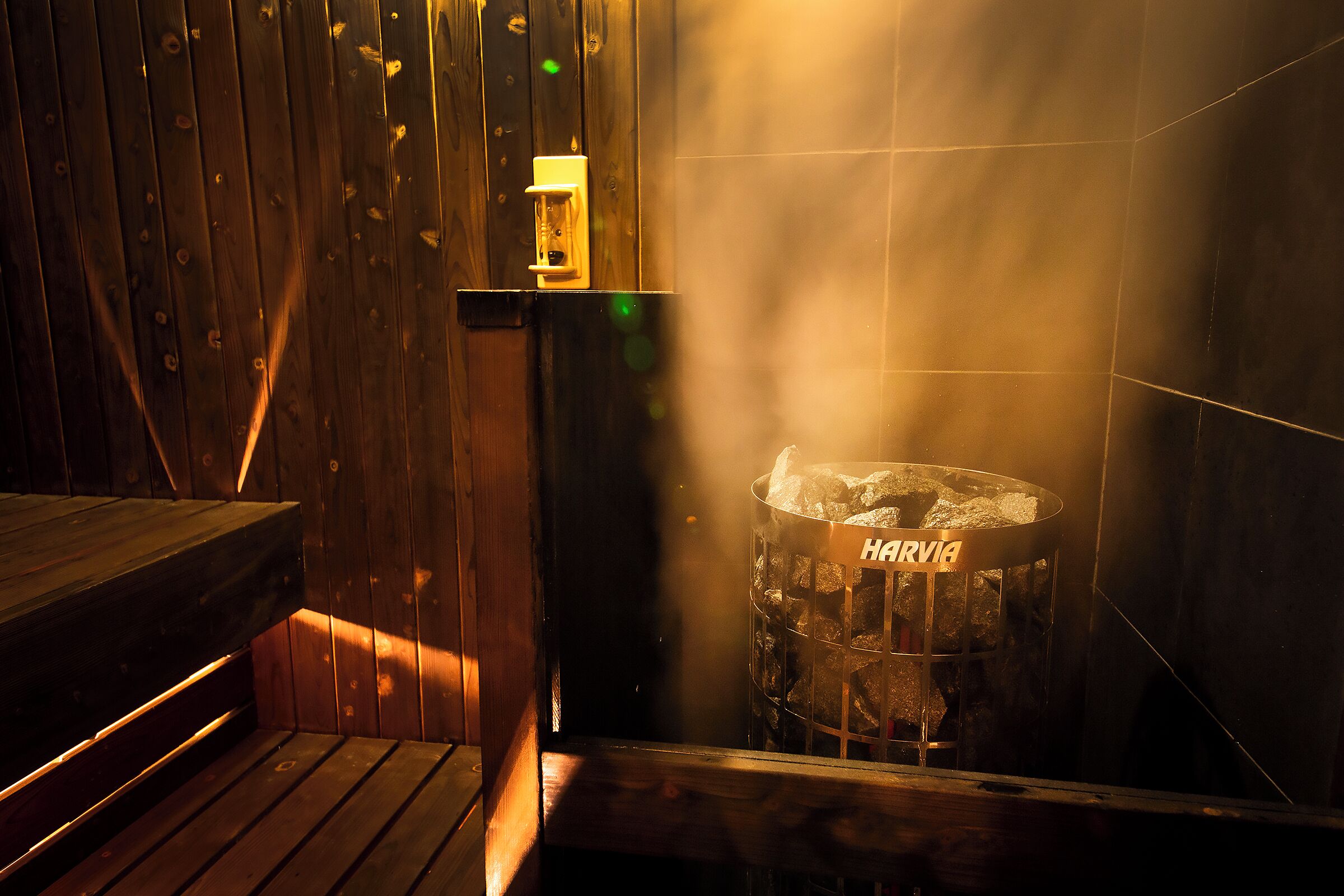 A wooden interior with a bench, a trash bin labeled "HARRIA", and a wall-mounted light fixture.