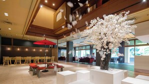 Un hall d’entrée spacieux agrémenté d’un grand arbre artificiel en fleurs de cerisier, de coins salon et d’un parapluie rouge.